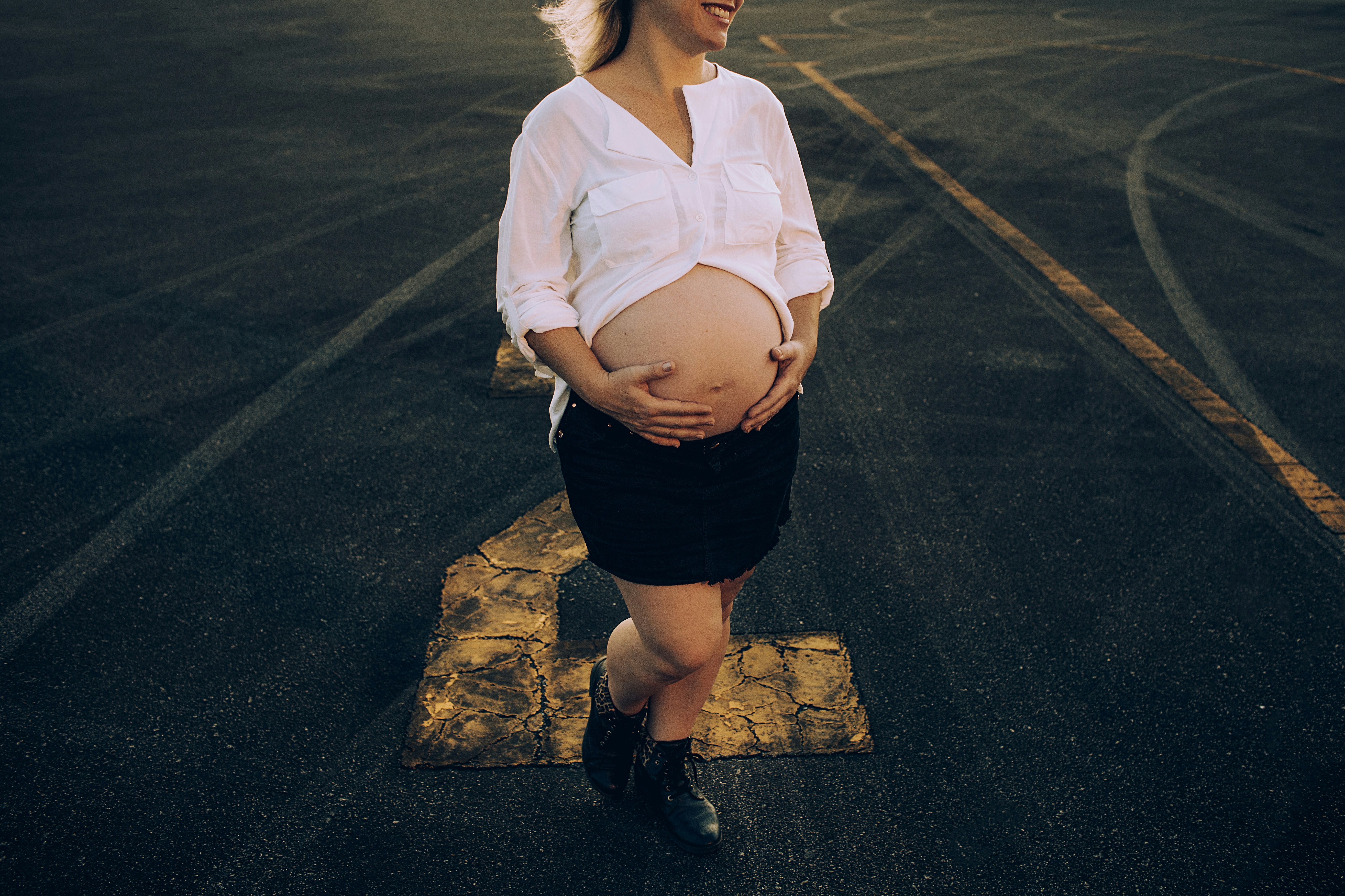 woman in white dress shirt and black skirt standing on gray asphalt road during daytime